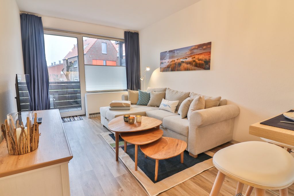 Düne 53 Grad Wohnzimmer mit beigen Cordsofa, Wohnzimmertischen und Balkon.