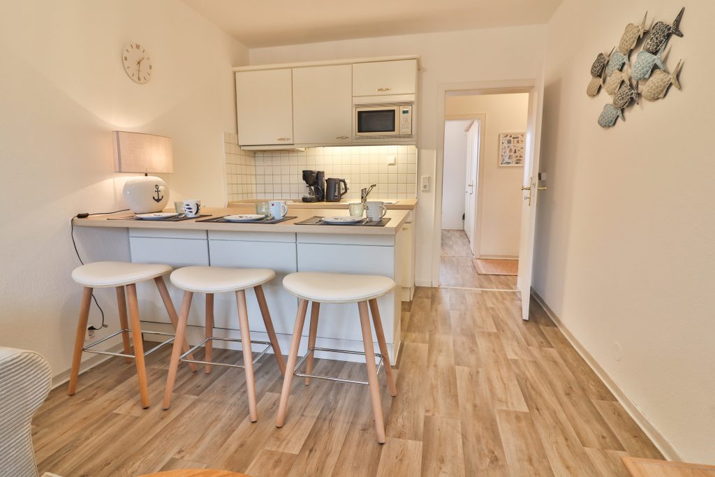 Düne 53 Grad hat eine weiße Küche mit Sitzgelegenheiten (Hockern), großer Lampe und liebevolles Geschirr.