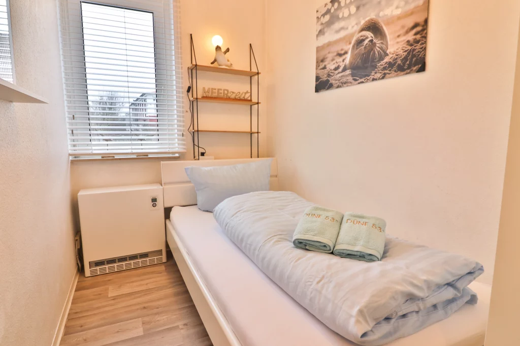 Das kleine Schlafzimmer der Düne 53 Grad hat ein kleines Bett, Nachttischlampen und Holzverdunkelungen am Fenster. Das Zimmer ist vor allem durch die Robbenbilder ideal für Kinder.